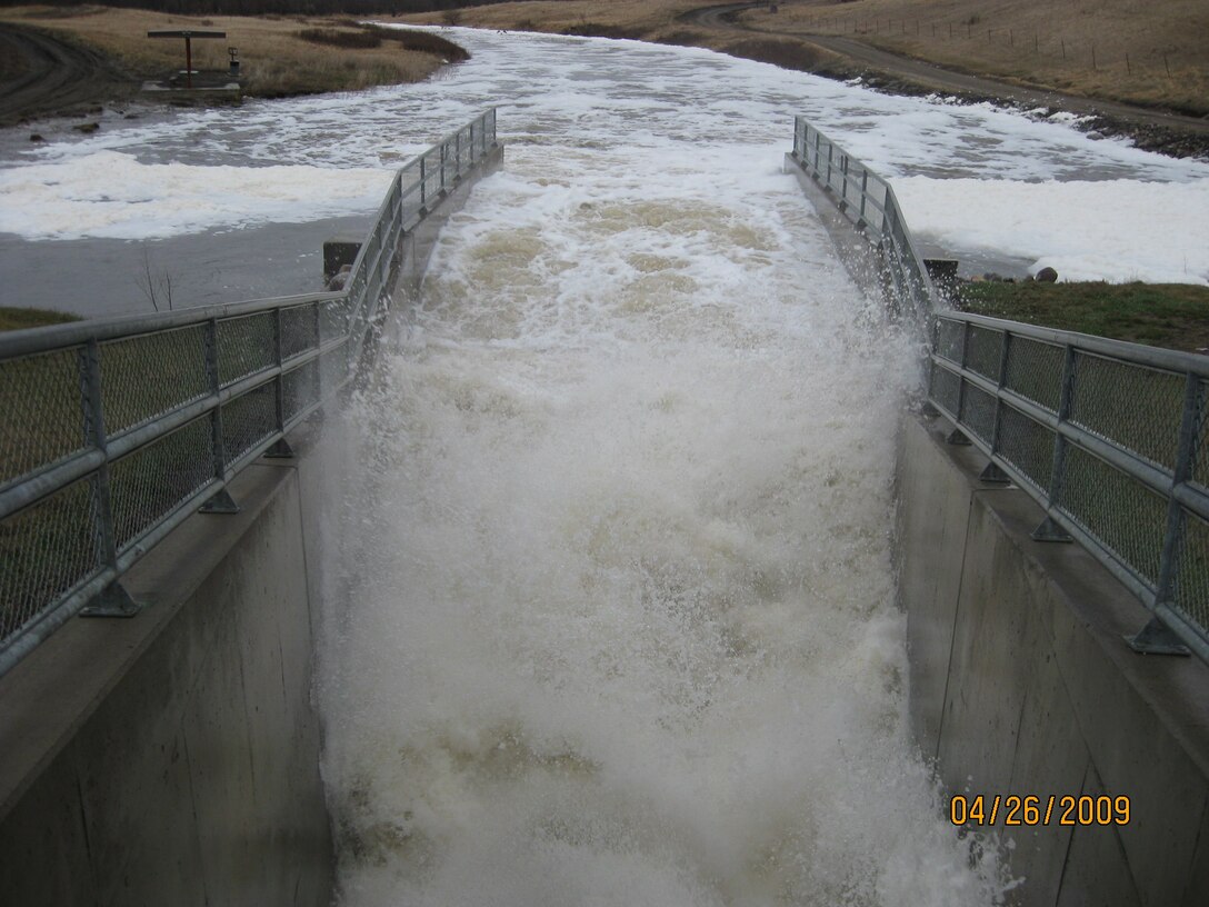 water flows through the Pipestem Dam outlet tunnel into a river