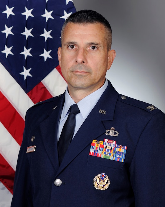 Official Air Force photo of man; looking at camera with U.S. flag and grey wallpaper background