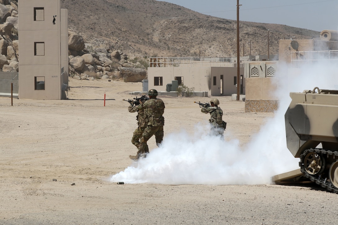 Soldiers run across desert terrain holding guns.