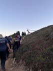 NAS Whidbey Island SAR crew members and ground rescue members move patient with broken ankle to an awaiting SAR helicopter.