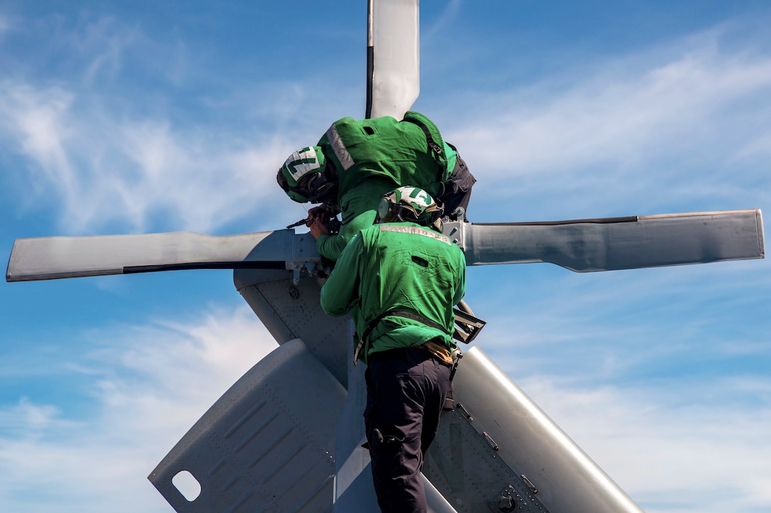 Two sailors perform maintenance on a helicopter.