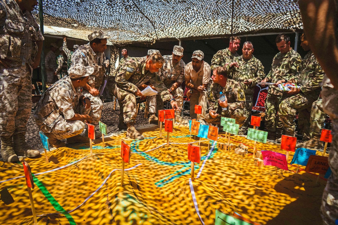 Troops in a tent gather around a table with colorful signs sticking out of it.