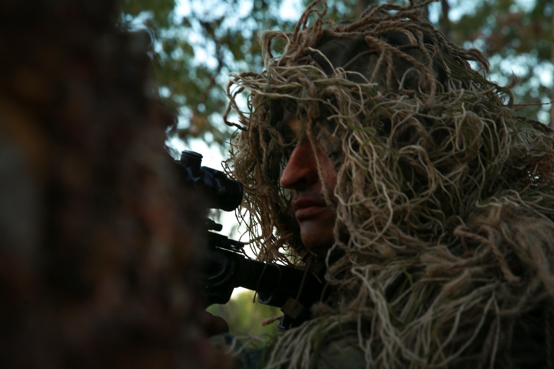 A Marine dressed in camouflage aims a weapon in the woods.
