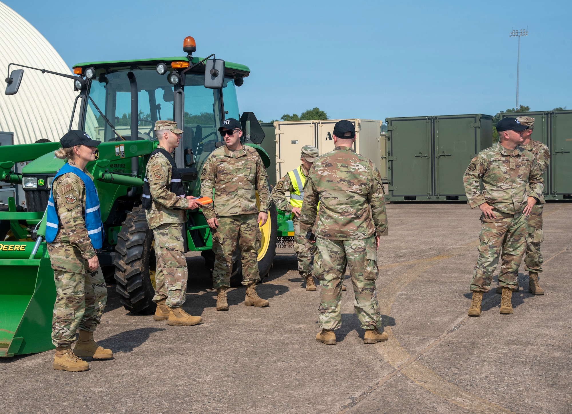 Members of a military inspection team stand in front of construction equipment.