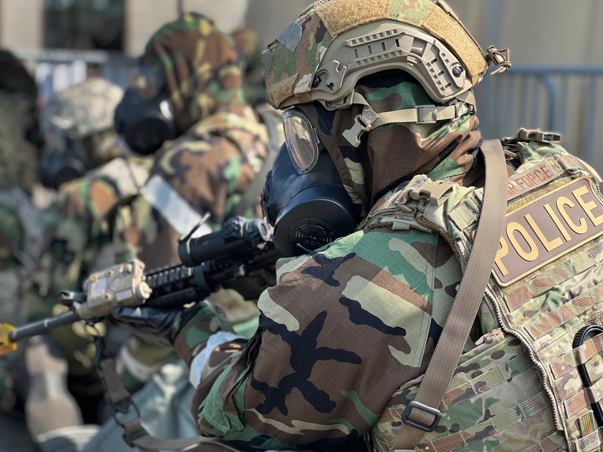 A man in  Mission Oriented Protective Posture (MOPP) gear and body armor holds a rifle.