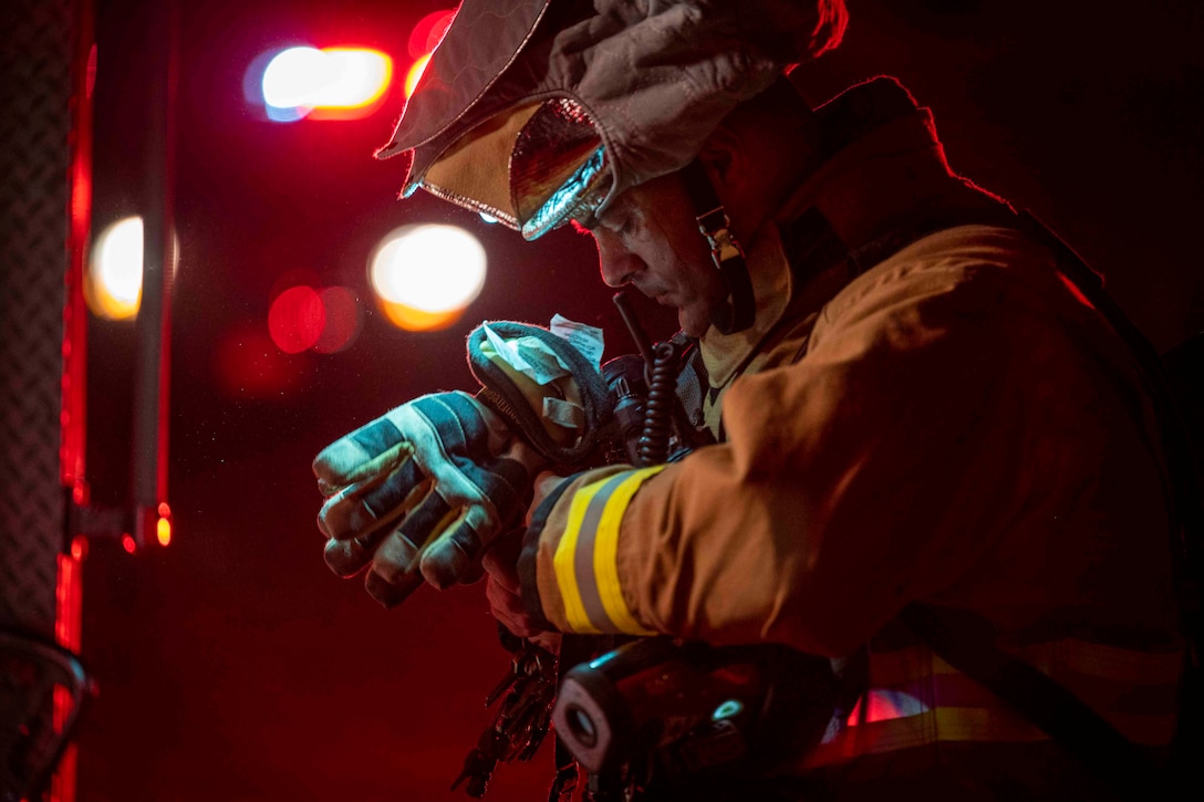 An airman wearing fire protection gear removes gloves from his hands.