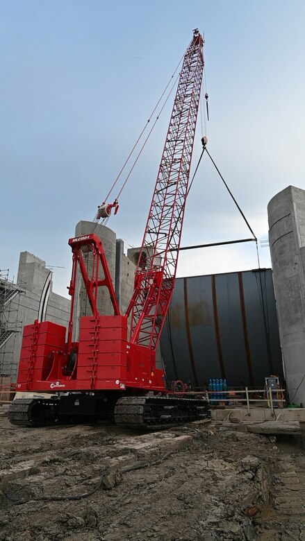 A red crane lifts a Tainter gate into position at a construction site.