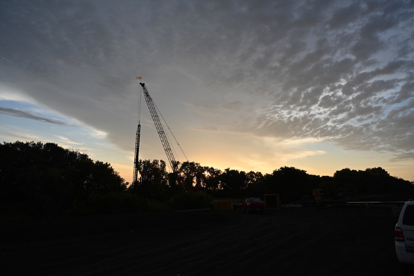 The sun rises early in the morning with a crane and trees in the foreground.