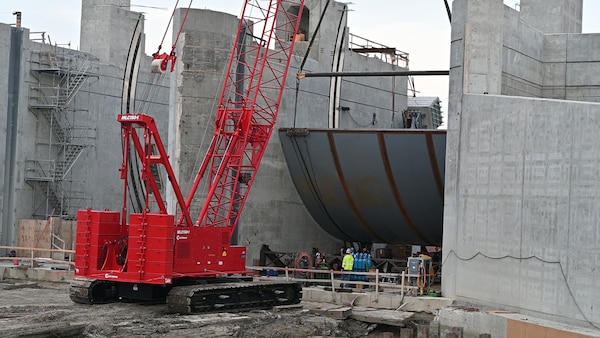 A red crane lifts a Tainter gate at a construction site