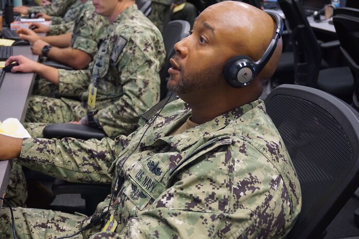 photo of US Military member sitting, wearing a headset working at a computer