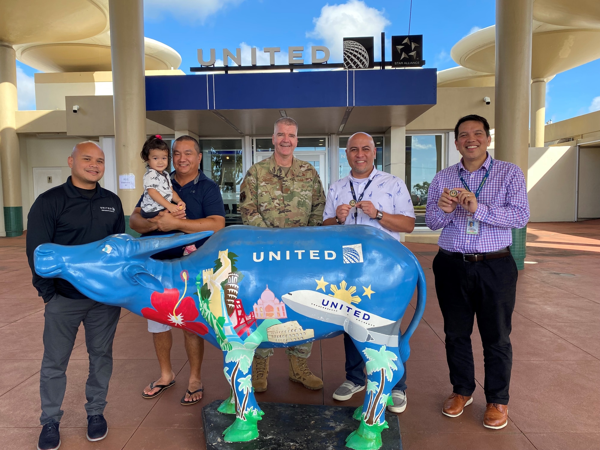 United Airlines workers and commander of 624 RSG stand behind United's colorful, painted bull, showcasing challenge coins earned for supporting Reserve Citizen Airmen.