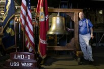 Retired Capt. Keith Larson stands next to the bell aboard USS Wasp