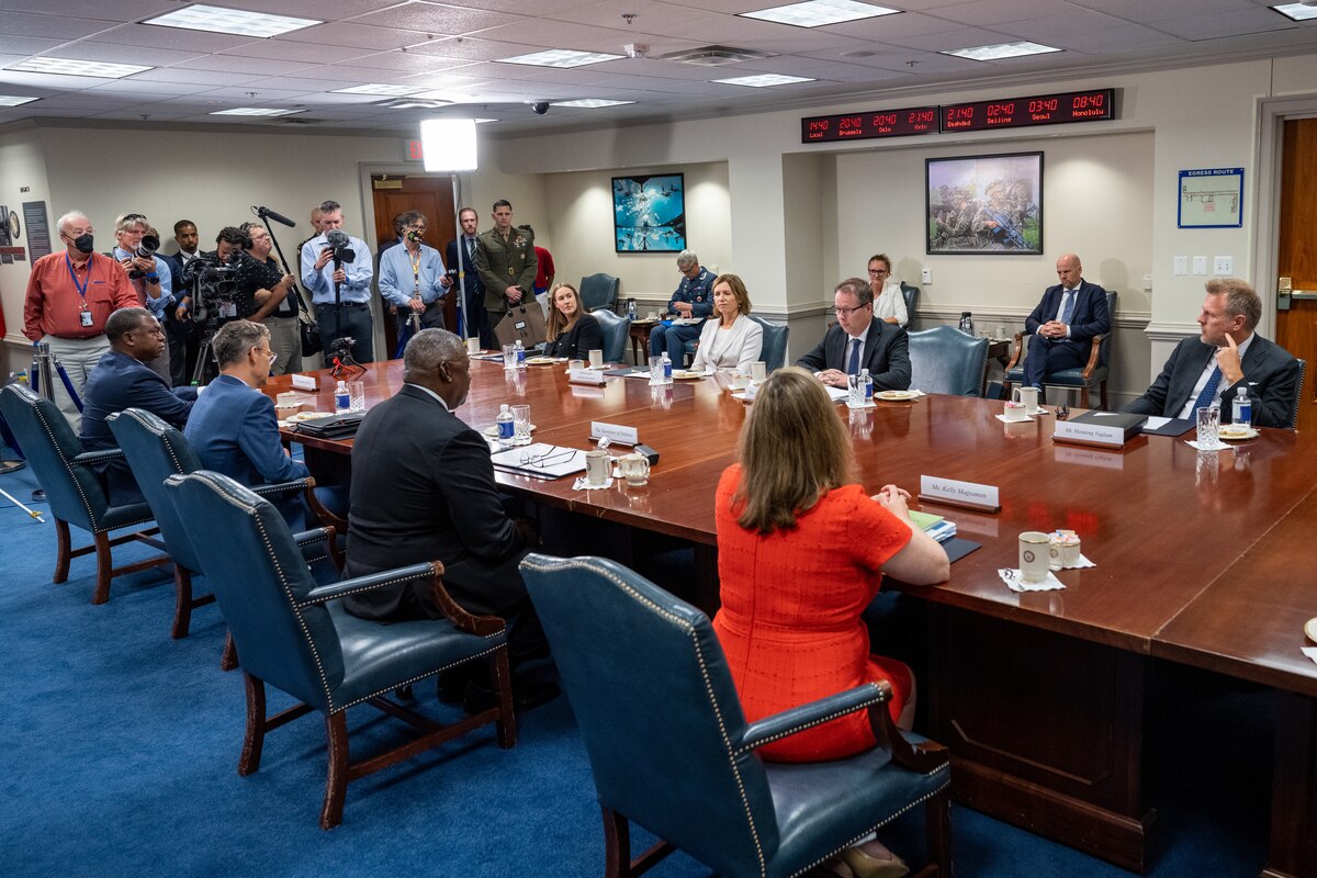 People sit a conference table as journalists film.