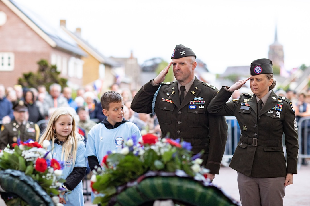 Two Army officers salute wreaths during a ceremony.