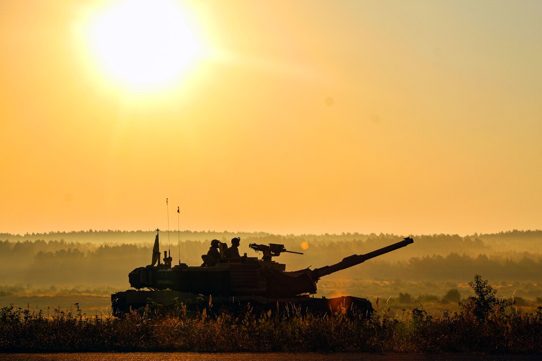 Two soldiers stand inside of a tank in a grass field.