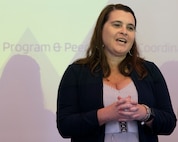 A woman speaks in front of a projector screen.