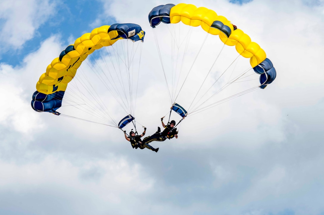 Two sailors perform with parachutes in the air.