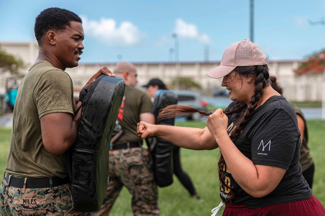 A Marine holds a punching bag as a woman punches it.