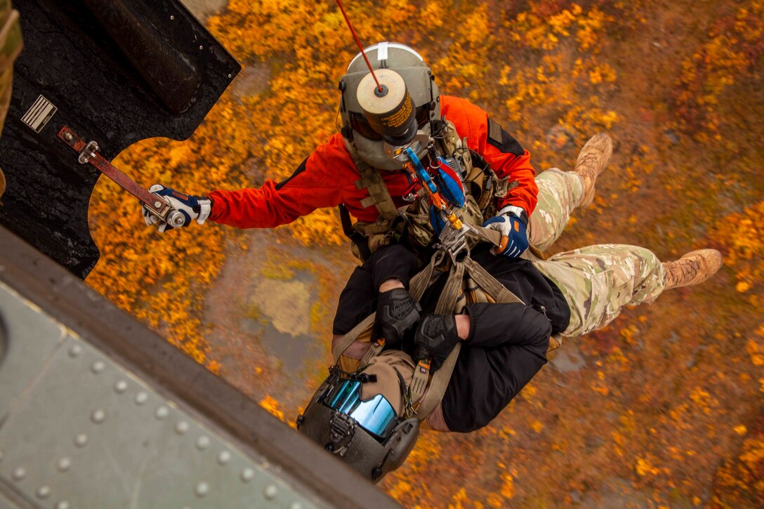 A guardsman hoists a person into an airborne helicopter.