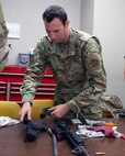 Male servicemember disassembling black rifle on table.