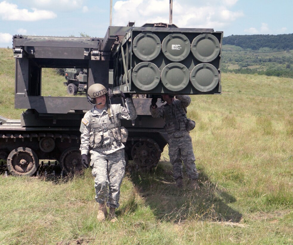 A service member stands near military rocket-launching equipment.