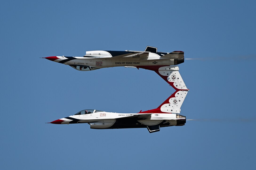 A red, white and blue-painted jet flies in blue sky, with an identical jet flying upside-down just above it.