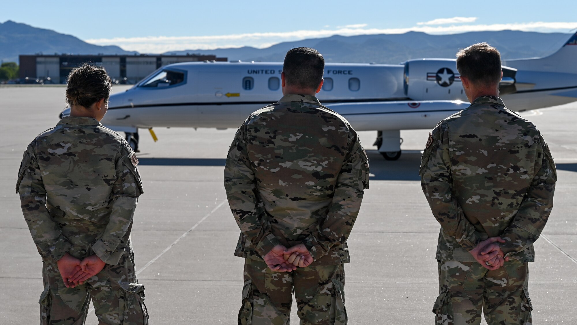 Three Airmen in uniform are shown from behind facing a plane