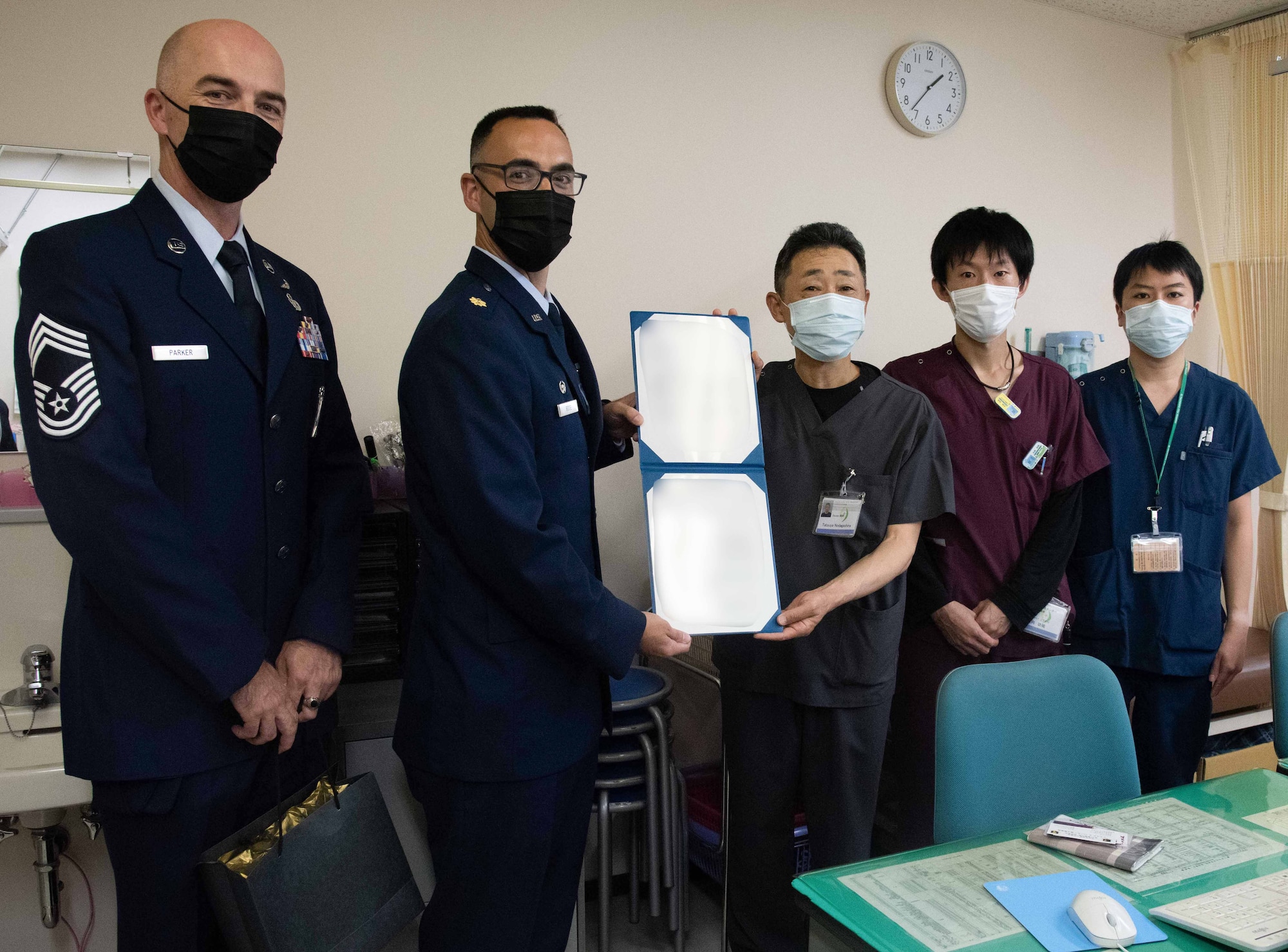 Military member and doctors pose for a picture holding an appreciation letter