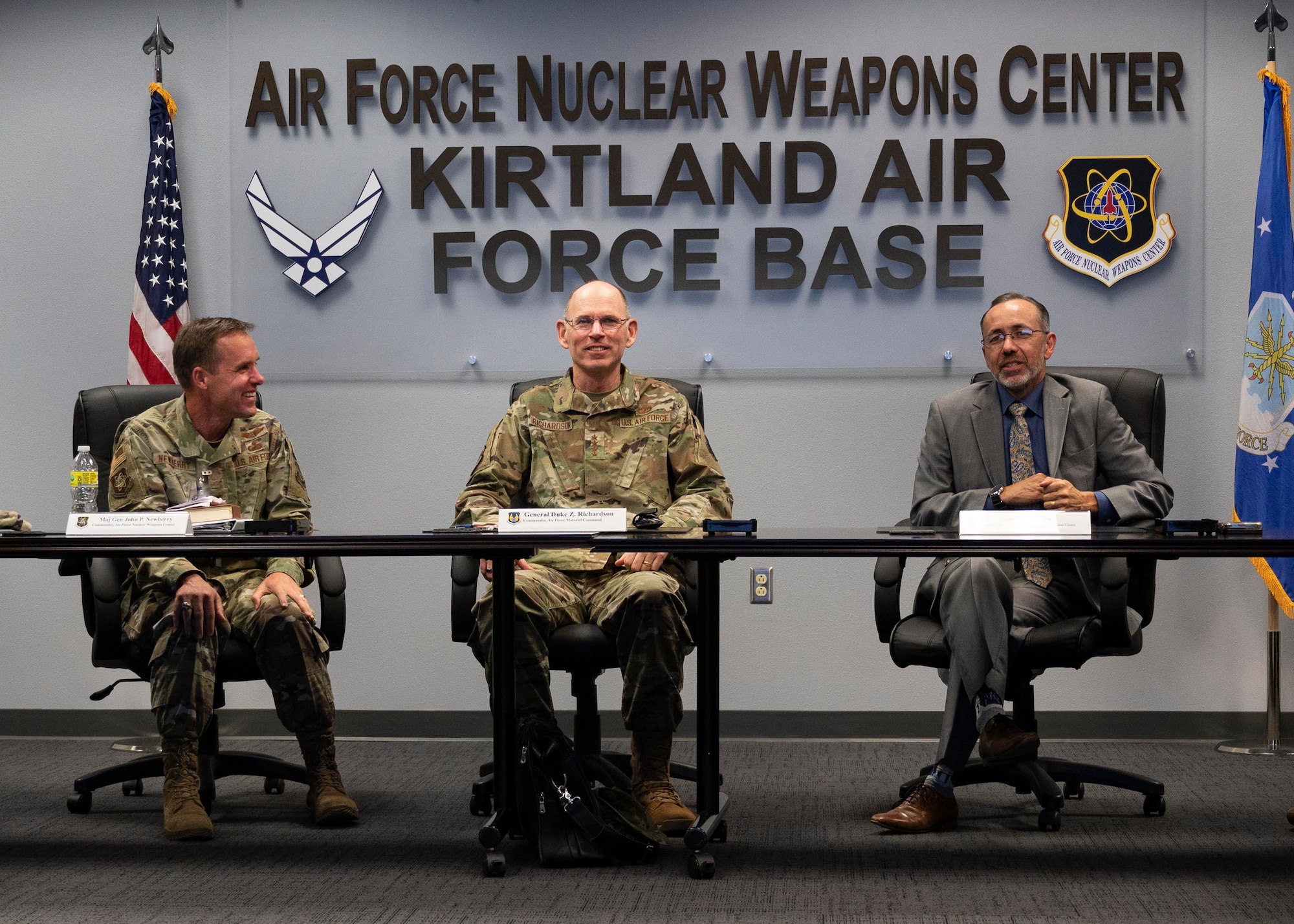 Two Airmen in uniform and one man in a suit sit at a conference table