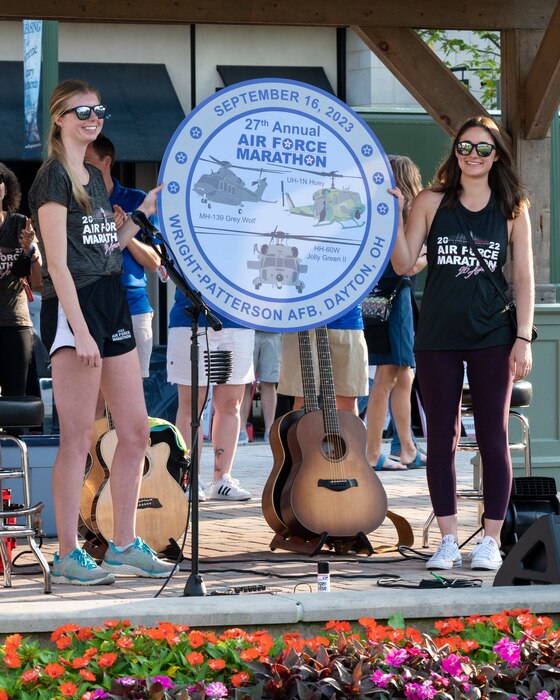Air Force Marathon staff members Chloe Fogle (left) and Rachel Nipper reveal the 2023 race medallion during an after-party Sept. 17 at The Greene in Beavercreek. The medallion features three Air Force helicopters. (U.S. Air Force photo by Jaima Fogg)