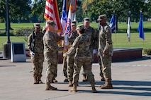 woman in u.s. army uniform holding flag passes it to man in uniform.
