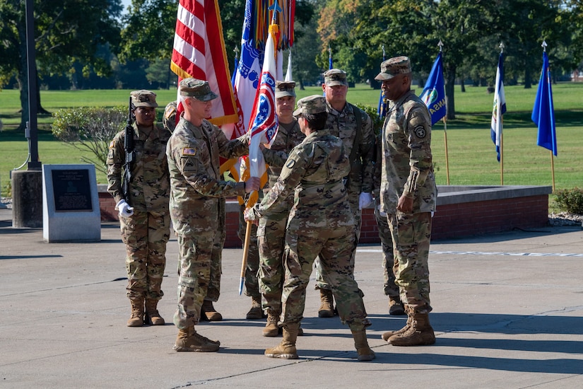 woman in u.s. army uniform holding flag passes it to man in uniform.