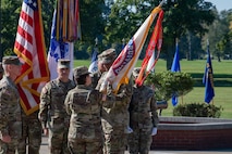 man in u.s. army uniform holding flag passes it to woman in uniform.