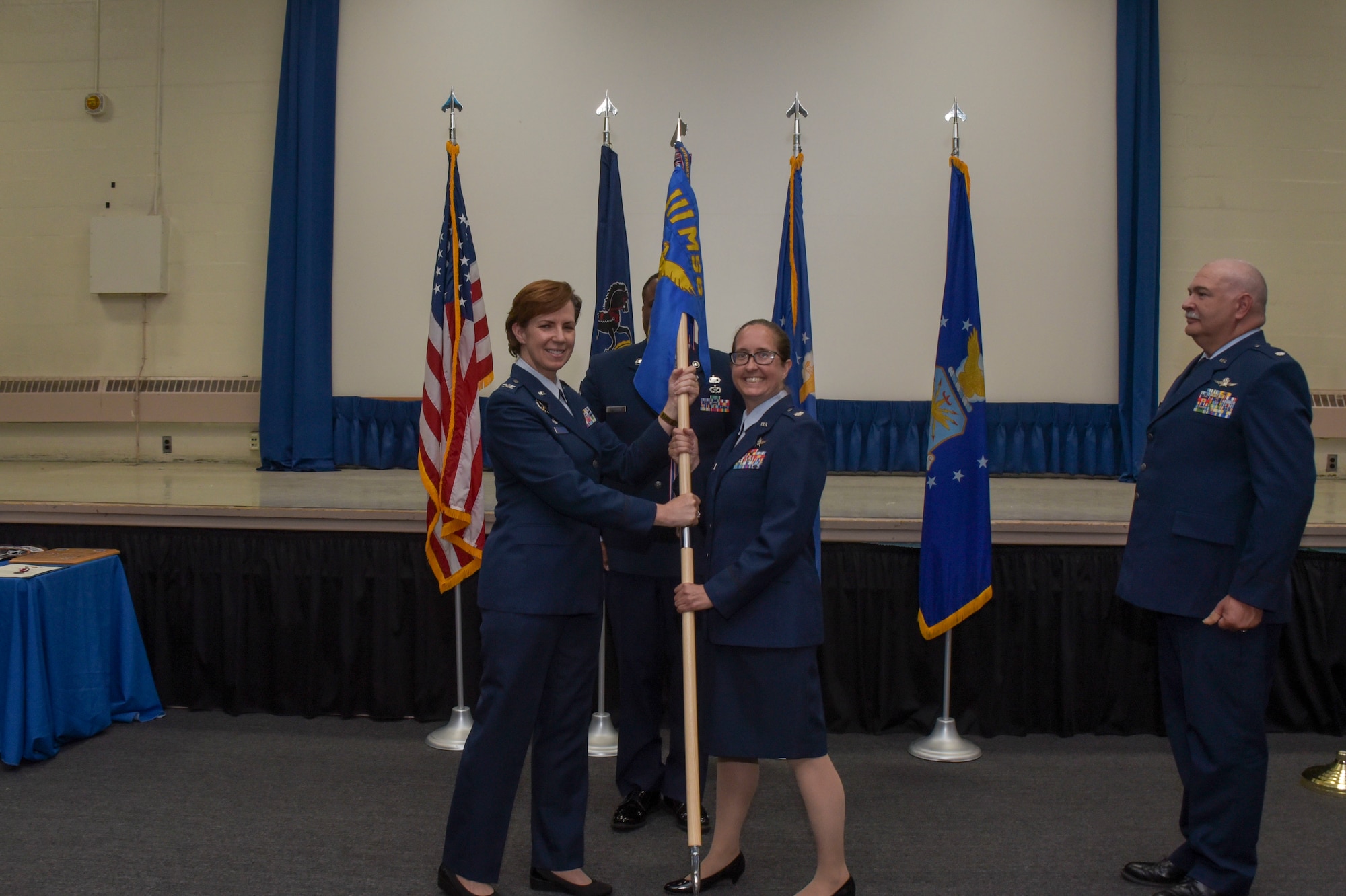 A woman in Air Force dress blues hands a unit flag to another woman in air Force dress blues.