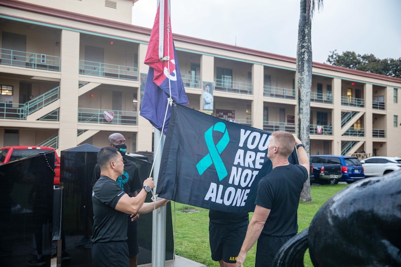 Two men place a flag on a flagpole as another man watches.