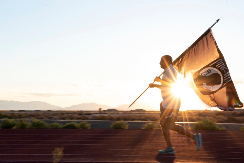 An airman runs on a track carrying a black flag with POW/MIA emblem.