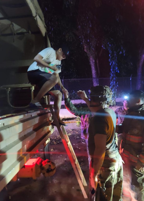 Guardsmen help a civilian in a military vehicle operating in floodwater.