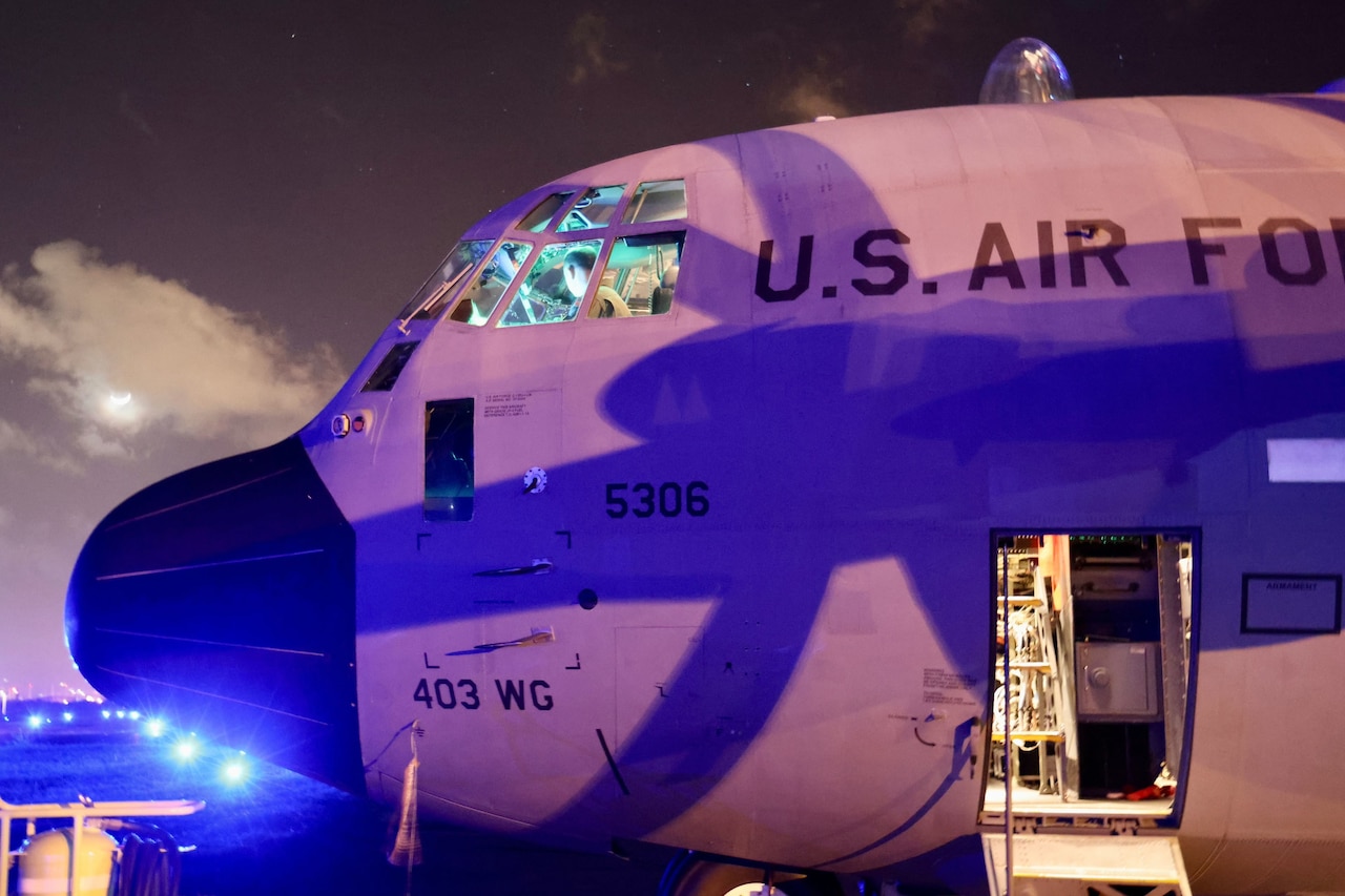 Front profile view of aircraft on a dark flightline, with cockpit illuminated.