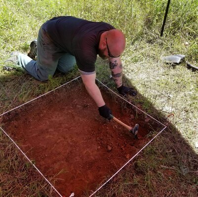 a man with a small tool working on a grid of earth in the ground.