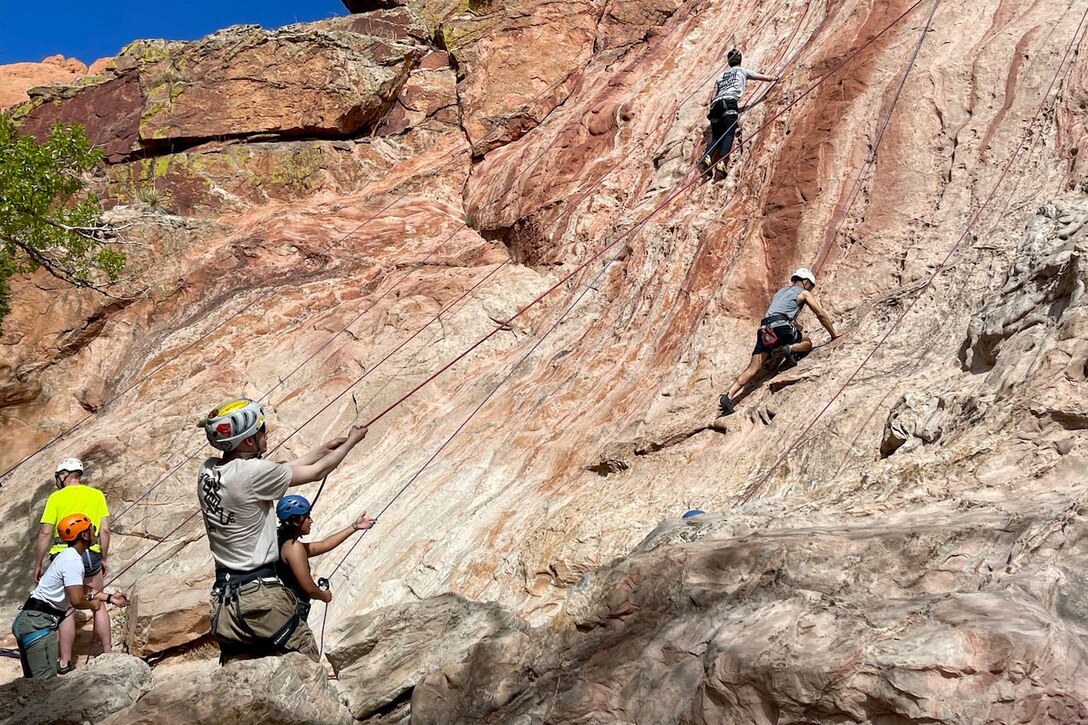 Soldiers climb a rock face.