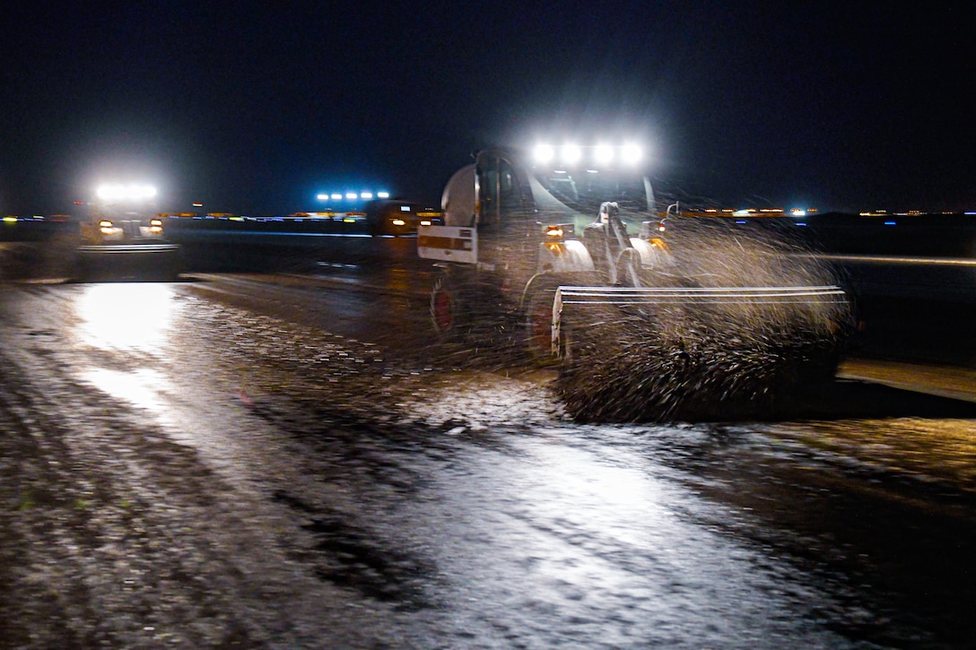 Vehicles remove rubber from a runway at night.
