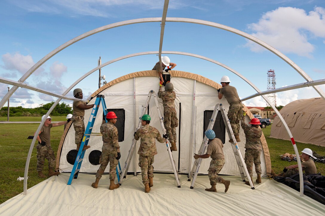 Airmen standing on ladders while building tents in a field.