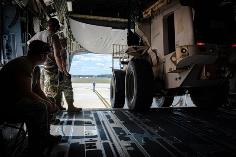 A group of airmen watch as a loader is driven off a ramp of a C-17 Globemaster