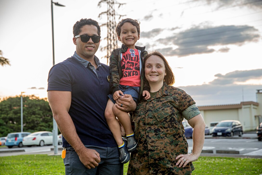 A man holds a child while a woman in uniform stands next to them.