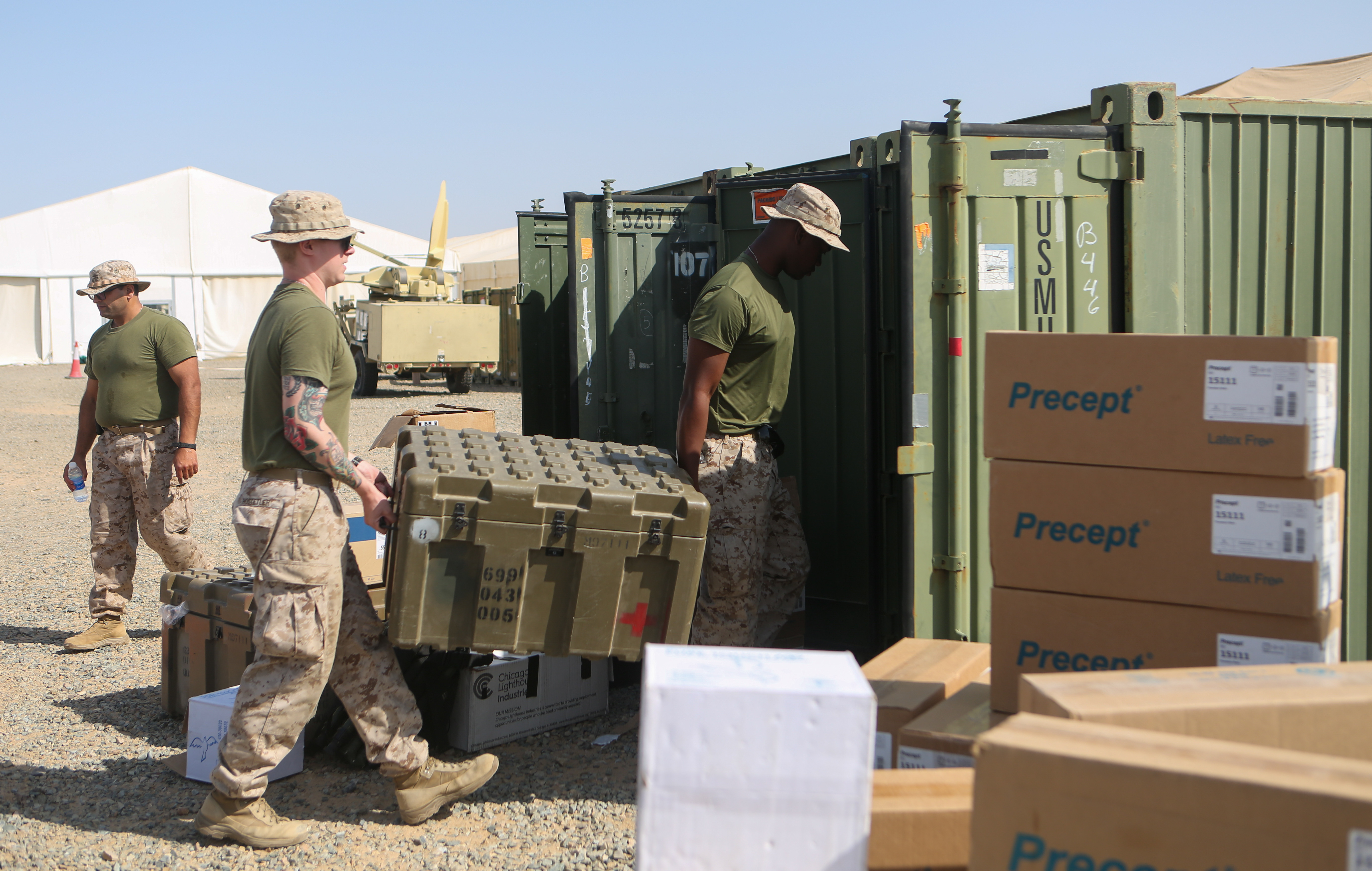 Two Marines carrying a large bin inside of a metal cargo container.
