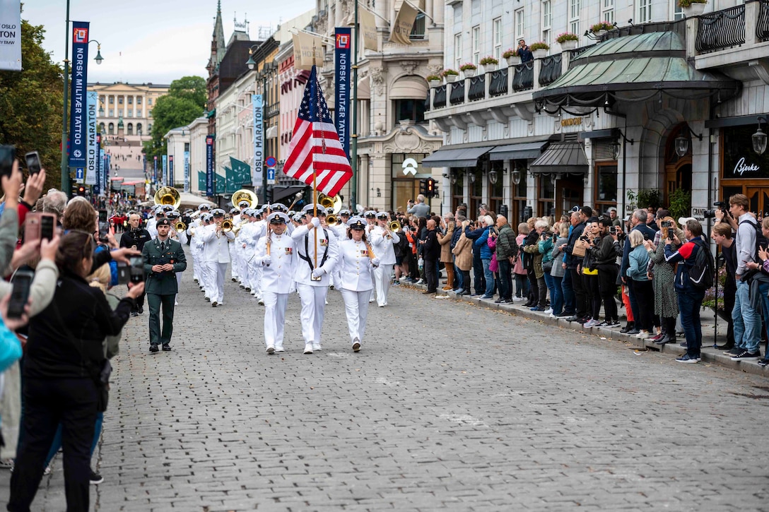 A military band walks down a street as a crowd stands on either side.
