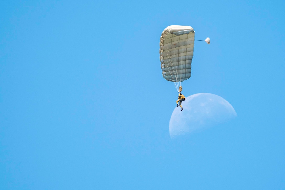 A sailor descends in the sky wearing a parachute as the moon shines in the background.