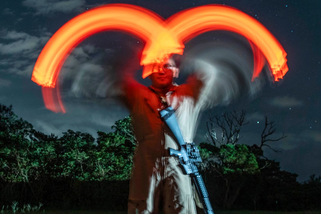 A Marine gives hand signals using red lights at night.