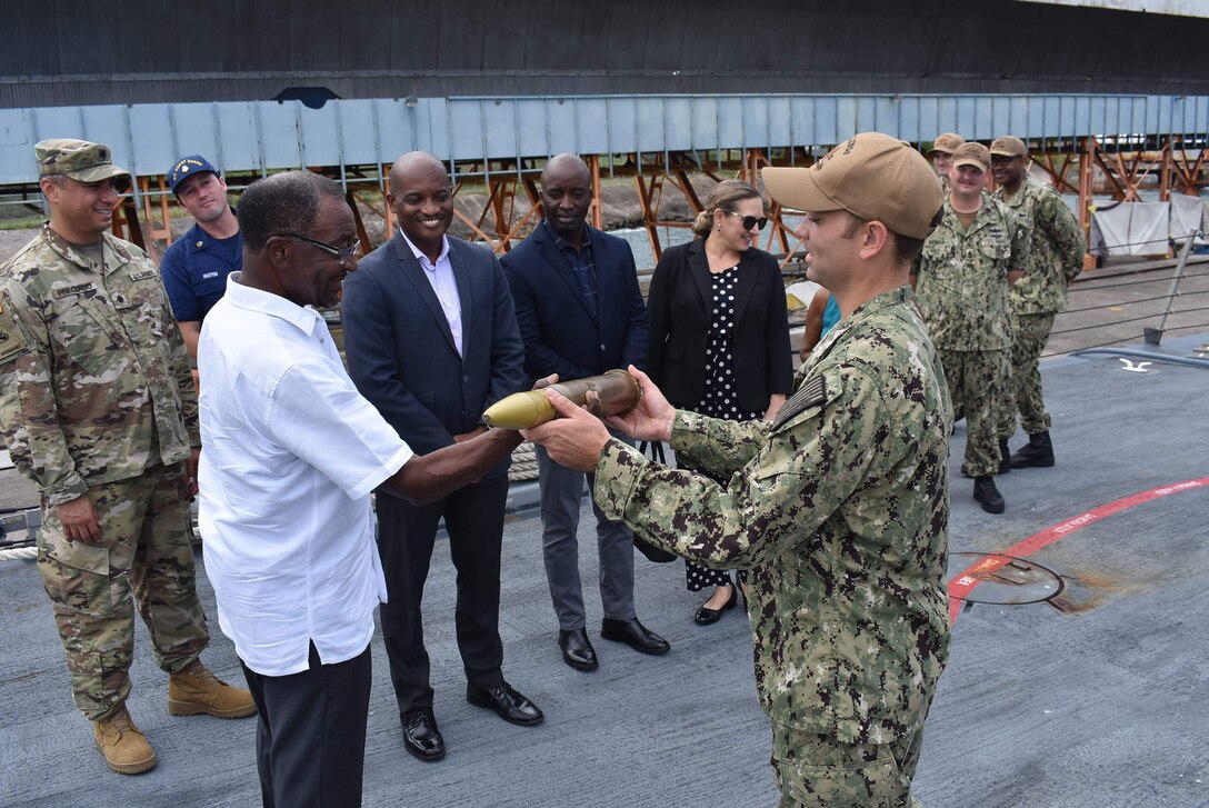 Chief Select Gunnar’s Mate Zach Morrill hands a simulated 57mm MK 110 round to U.S. Ambassador to Jamaica, Noah “Nickolas” Perry aboard the Freedom-variant littoral combat ship USS Billings (LCS 15) during a scheduled port visit in Ocho Rios, Jamaica, Sept. 17, 2022. Billings is deployed to the U.S. 4th Fleet area of operations to support Joint Interagency Task Force South’s mission, which includes counter-illicit drug trafficking missions in the Caribbean and Eastern Pacific.