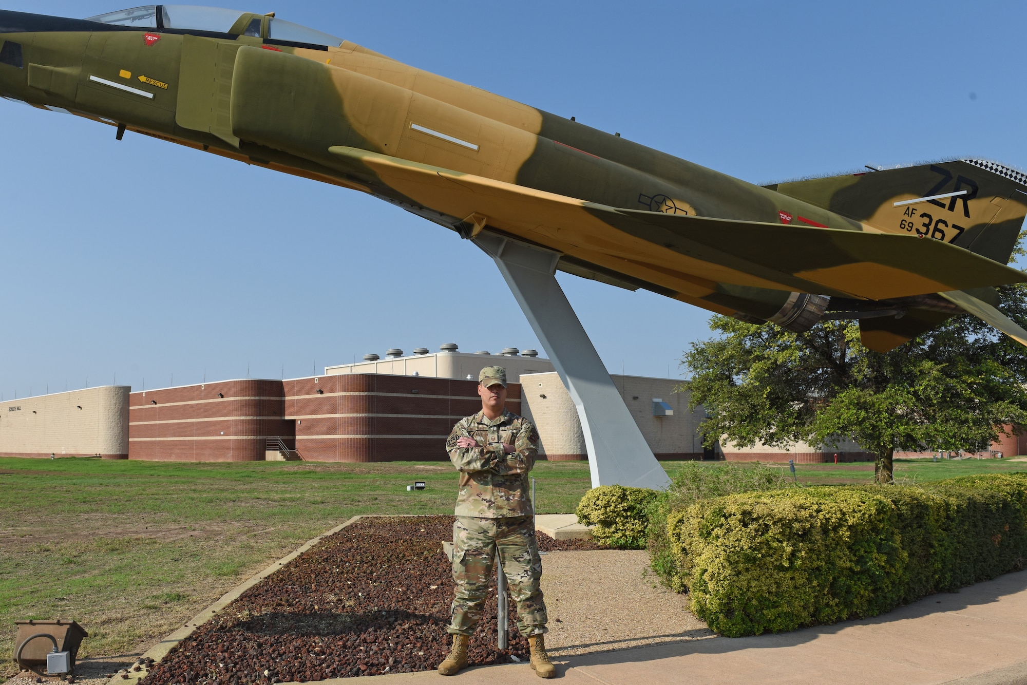 U.S. Air Force Master Sgt. Mickey Bretado, 313th Training Squadron flight chief, poses for a photo next to a RF-4 aircraft static display at Goodfellow Air Force Base, Sept. 12, 2022. The RF-4 was equipped with a variety of film-based and side-looking radar, and it was an unarmed photographic reconnaissance version of the F-4C aircraft. (U.S. Air Force photo by Airman 1st Class Zachary Heimbuch)